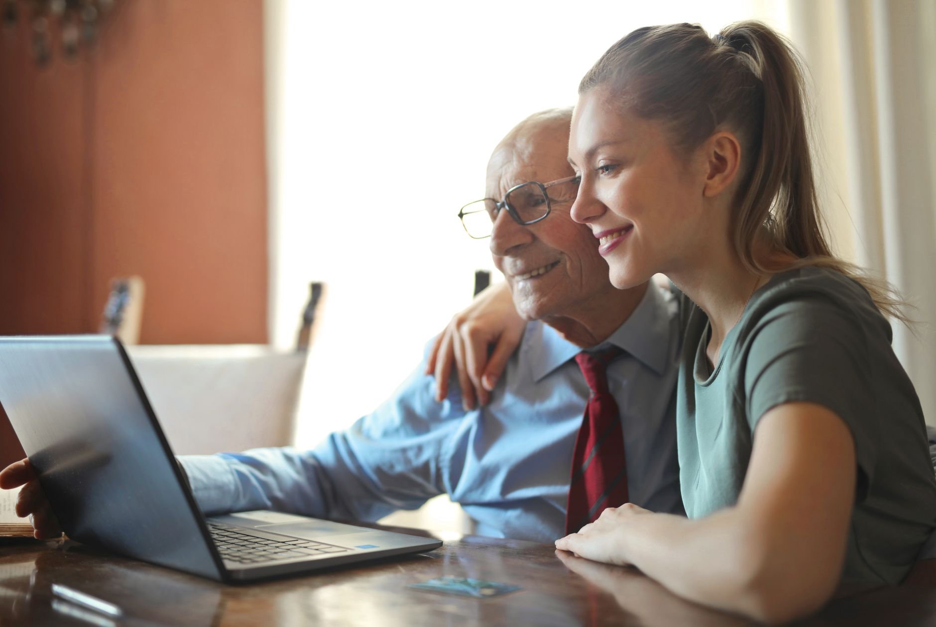 A younger woman helping an older man use a laptop at a table